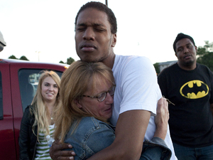Judy Goos, second from left, hugs her daughters friend, Isaiah Bow, 20, while eye witnesses Emma Goos, 19, left, and Terrell Wallin, 20, right, gather outside Gateway High School where witness were brought for questioning after the shooting at the premiere of the new Batman film in Colorado