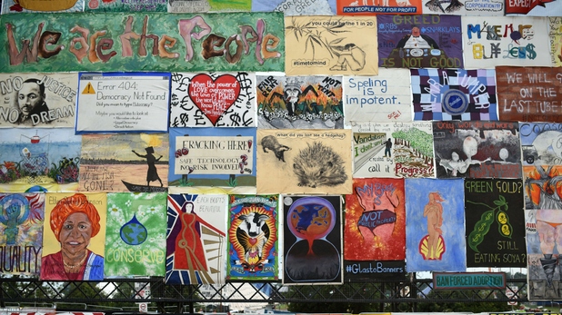 Revellers walk past an array of political and environmentally themed posters at Glastonbury Festival 2015